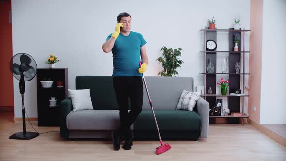 A male cleaner stands with his elbows on the brush talking on the phone alt
