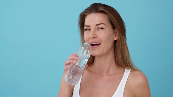 Beautiful Blonde Woman Wearing a White Top Drinking from a Bottle of Water