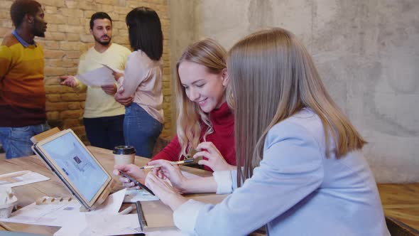 Female Designers Discussing Interior Plan while Colleagues Talking in Office