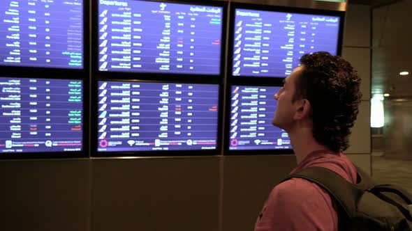 Frustrated Man Standing Near Airport Timetable and Looking at Cancelled Flights, Travel Frustration