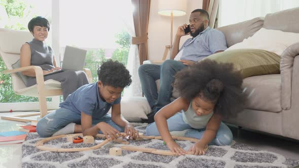 Happy African family father and mother working and children doing activity playing toy railway. alt