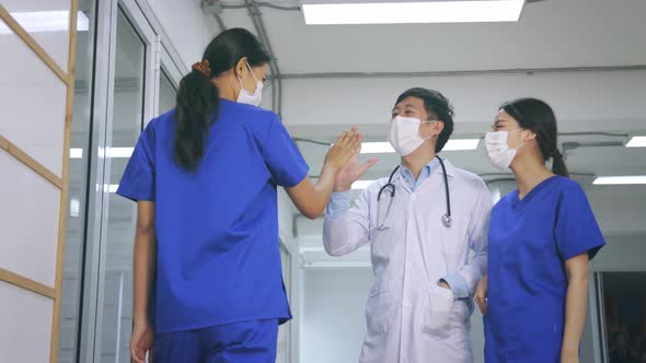 Happy Young Asian Team of Doctor and Nurse in Uniform with Stethoscope and Mask Giving High Five alt