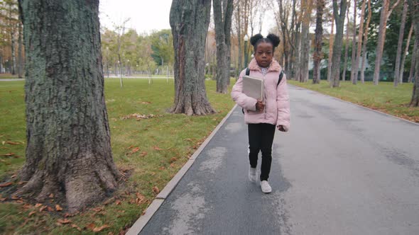 Little African American Girl Going to School in Park Pupil Holding Book in Hand Concentrated Kid alt