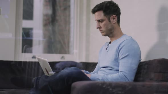 Adult male sitting on sofa at home working laptop