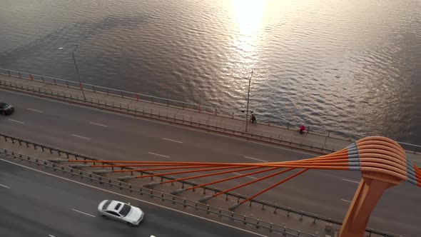 Aerial Orbit Shot: Two People Ride Bicycles Along Bridge alt