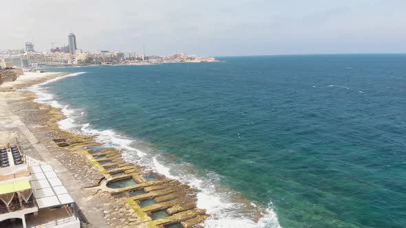 Sliema rocky seascape blocked by Promenade and city skyline, in Malta - Revealing Pan aerial alt