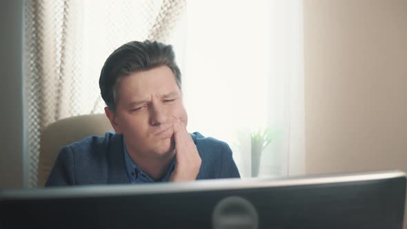 Man Having Toothache While Sitting at Computer alt