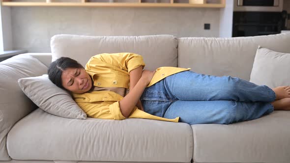 Young AfricanAmerican Woman Sitting on the Couch and Suffers From Stomach Cramps