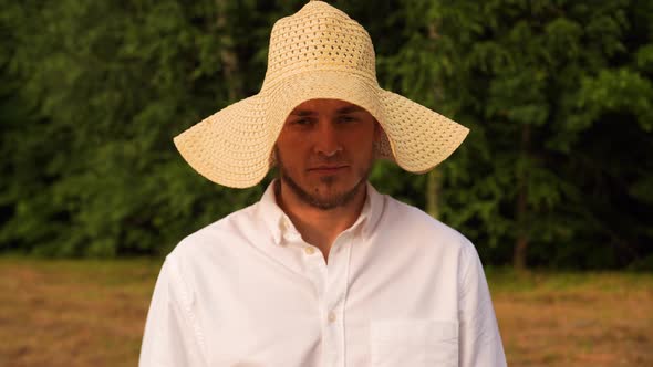 Guy in Straw Yellow Hat is Standing in a Field Looking Seriously at the Camera
