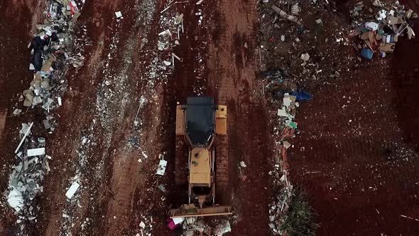 A bulldozer pushes trash at a landfill site - aerial straight down view alt