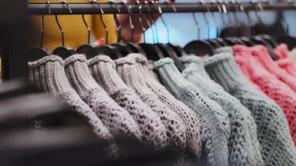 Closeup Clothes Hanger with Colored Sweaters in Clothing Store Female Hands Sorting Clothing alt