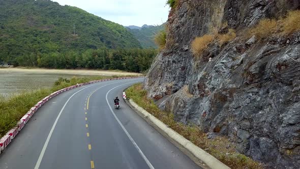 Woman on a moped riding on an island road near the coastline, Aerial follow behind shot alt