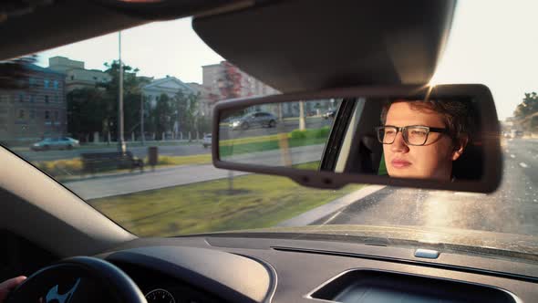 Adult Man in Eyeglasses Is Driving a Car Reflection in Rearview of Car