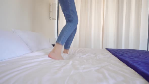 an unrecognizable woman without face with bare feet jumps on bed in bedroom alt