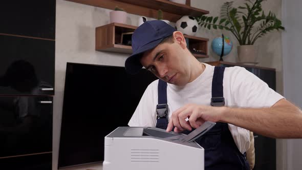 A Male Handyman in Blue Overalls Inspects a Printer Before Starting Repairs alt