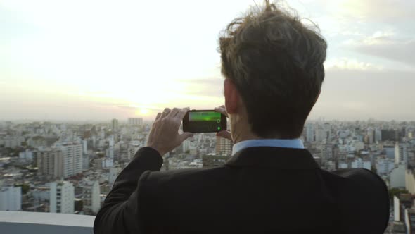 Rear view of businessman taking picture of city with smartphone