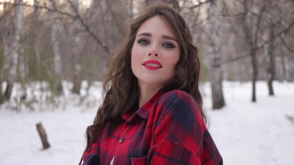 Young Woman with Wavy Hair Standing and Touching Face in Winter Forest