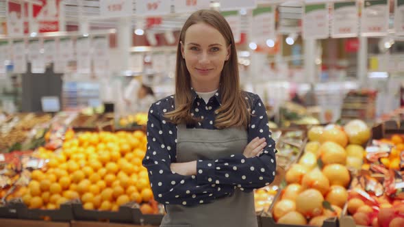 Portrait of a Female Worker in an Apron Against a Background of Fruits a Young Woman Crosses Her alt