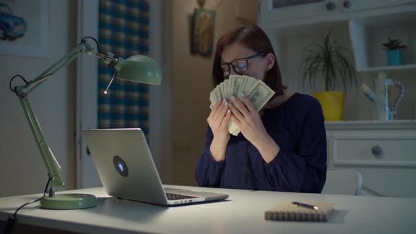 30s working from home woman counting dollars money cash and smelling money alt
