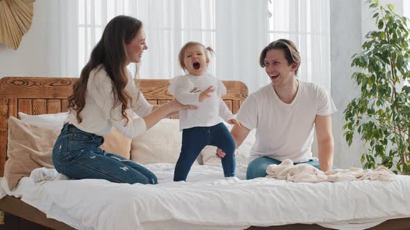 Happy Family Young Parents with Baby Small Daughter Have Fun Playing Jumping on Bed Cozy Bedroom alt