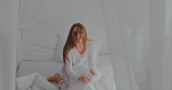 Girl in Pajamas is Having Fun in the Bedroom Jumping on the Bed and Throwing White Pillows