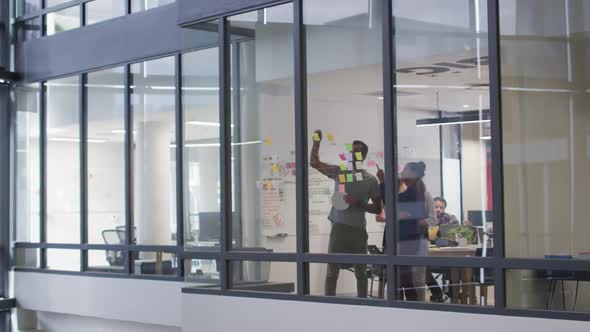 Diverse male and female work colleagues brainstorming using glass wall in meeting room alt