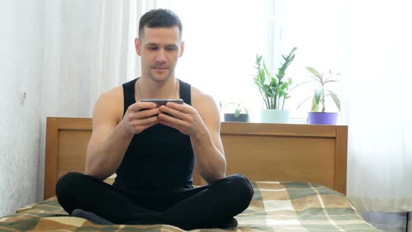 Attractive Young Man Uses Smartphone While Sitting on the Couch