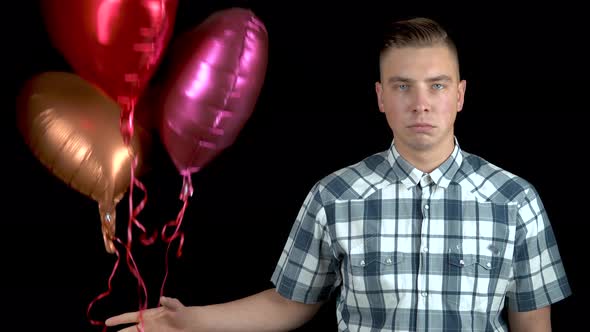 Sad Young Man Let Go of Heart-shaped Balloons. A Sad Man Stands with Helium Balls on a Black alt