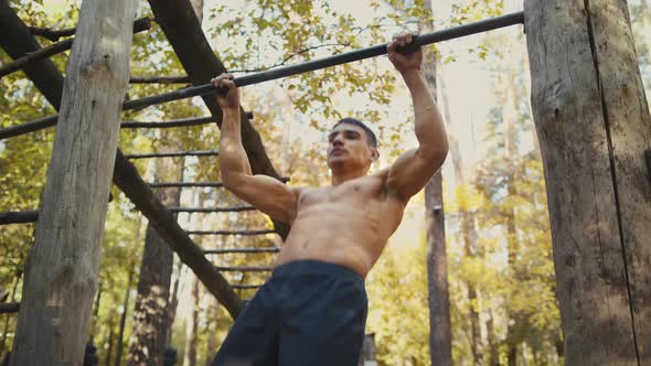 Man is doing pull ups exercises on horizontal bar in the forest gym, outdoors