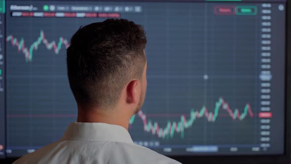 Man trader looking at graph currency money at screen indoors. Male businessman person check money