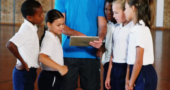 Sports teacher and school kids using digital tablet in basketball court alt