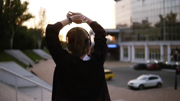 Footage of a Stylish Girl Dancing Outdoors on the Street with Modern Building on the Background alt