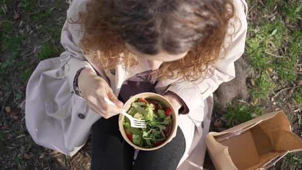 Woman Sits on Grass in City Park Eating Fresh Vegan Salad alt