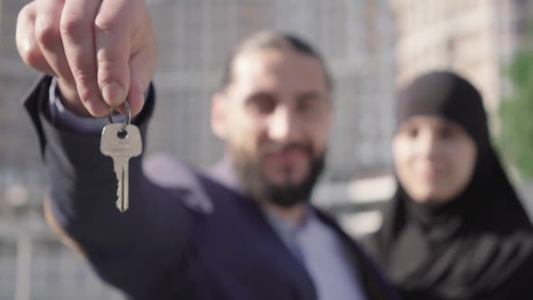 Close-up of Key in Male Hand with Blurred Middle Eastern Couple Smiling at the Background. Happy alt