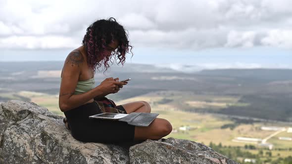 Woman Seen Sitting on Edge of Mountain Using Her Cellphone