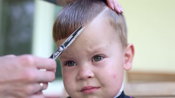 Emotions on Little Boy's Face While Hairdresser's Hand with Scissors Cutting His Hair on Fringe alt