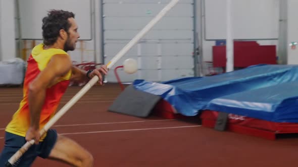 Pole Vaulting Indoors - a Man in Yellow Shirt Running Up and Jump Over the Bar alt