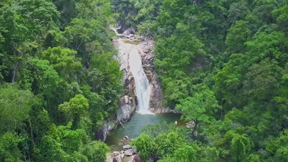 Flycam Approaches Waterfall Streaming Into Lake Among Landscape