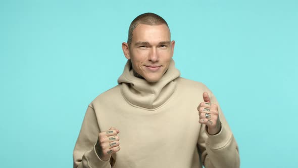 Attractive Young Man 20s with Tattoos on Shaven Head and Hands Wearing Hoodie Dancing and Smiling at