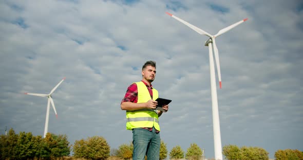 The Engineer Work Next to the Windmill Turbines with the Tablet in His Hand alt