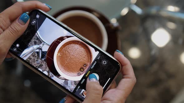 Close Up of Woman Holds Modern Smartphone and Taking Pictures of Cocoa to Share Photos on Social