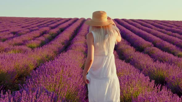 Young Woman in White Dress Walking Through a Lavender Field on Sunset