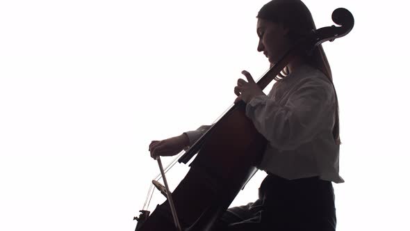 Silhouette of a Girl Playing the Cello on a White Background in the Studio alt