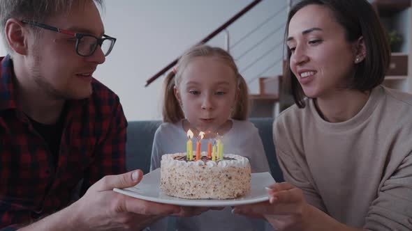 Mother and Father Holding Small Birthday Cake While Daughter Blo