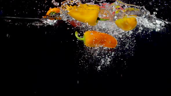 Colorful sweet peppers being dropped into water in slow motion. alt