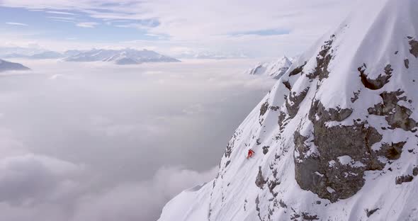 Aerial drone view of a skier skiing down a steep snow covered mountain. alt