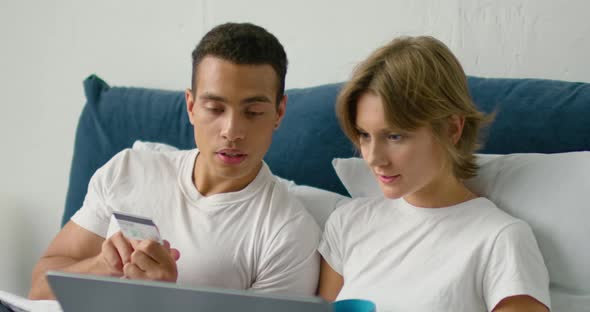 Young Mixed Race Couple Is Making Online Purchase, Lying in a Bed alt