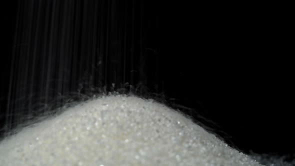 White Granulated Sugar Pours Onto a Black Glass Surface Creating a Slide alt