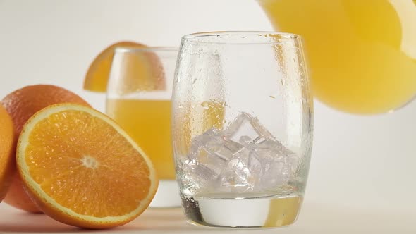 Pouring Orange Juice Into Glass From Jug. Glass of Orange Juice with Ice Cubes alt