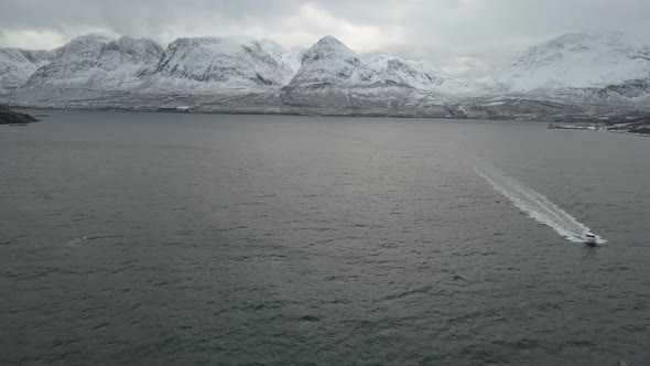 Cinematic drone shot crossing in front of racing speedboat in ocean, snowy mountain background alt